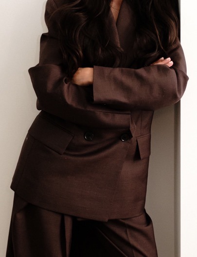 Cropped editorial photograph showing the editor’s folded arms in a brown suit